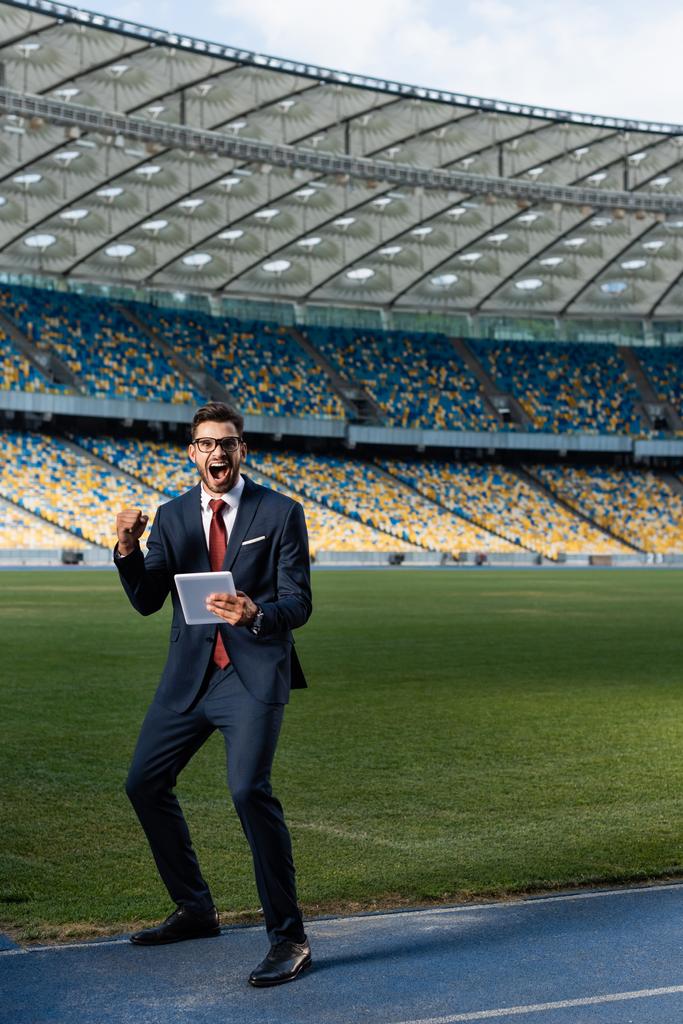 giovane uomo d'affari in giacca e cravatta utilizzando tablet digitale e mostrando yeas gesto allo stadio, concetto di scommesse sportive
 - Foto, immagini