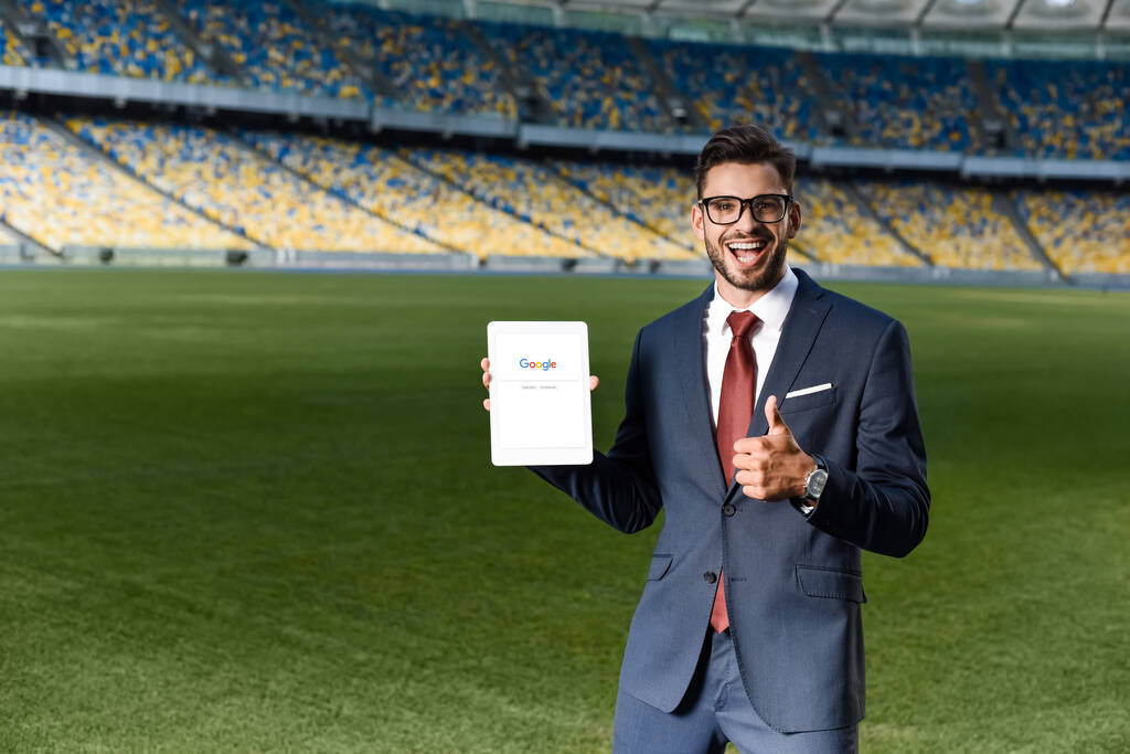 KYIV, UCRAINA - 20 GIUGNO 2019: giovane uomo d'affari felice in giacca e cravatta con tablet digitale e google app e con il pollice alzato allo stadio
 - Foto, immagini