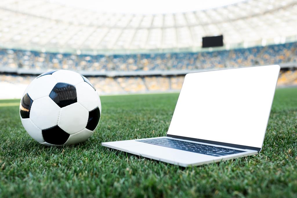 fotbalový míč a notebook s prázdnou obrazovkou na travnatém fotbalovém hřišti na stadionu - Fotografie, Obrázek