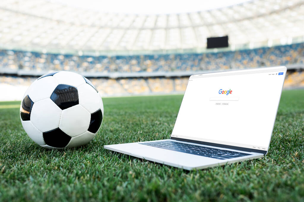 KYIV, UCRANIA - 20 de junio de 2019: pelota de fútbol y portátil con el sitio web de google en el campo de fútbol herboso en el estadio
 - Foto, imagen