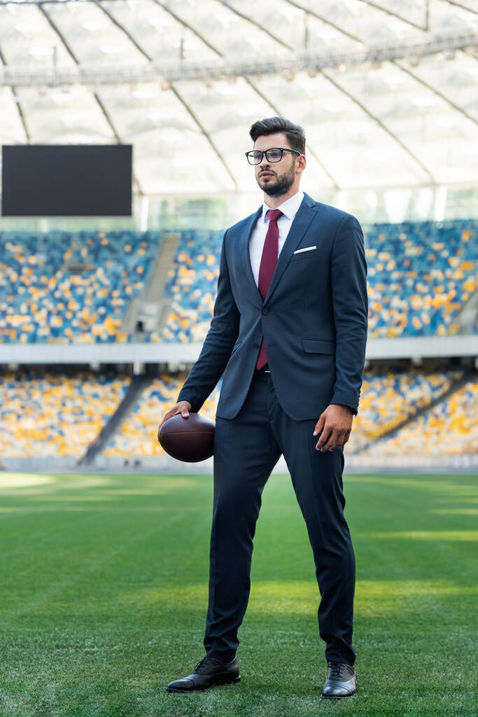 młody biznesmen w garniturze i okulary z piłką rugby na stadionie - Zdjęcie, obraz