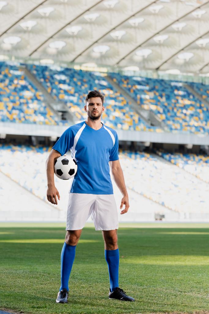 プロのサッカー選手が青と白のユニフォームを着てスタジアムのサッカーピッチでボールを持ち - 写真・画像