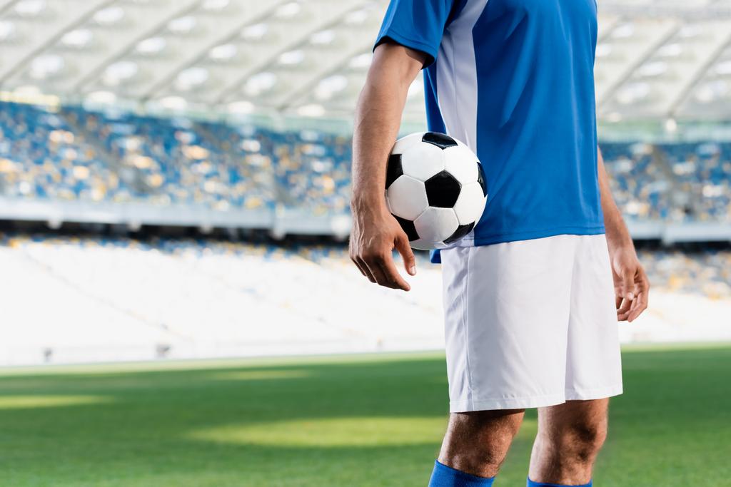 プロのサッカー選手を青と白のユニフォームで切り取り スタジアムのサッカーピッチでボールを持っている ロイヤリティフリー写真 画像素材