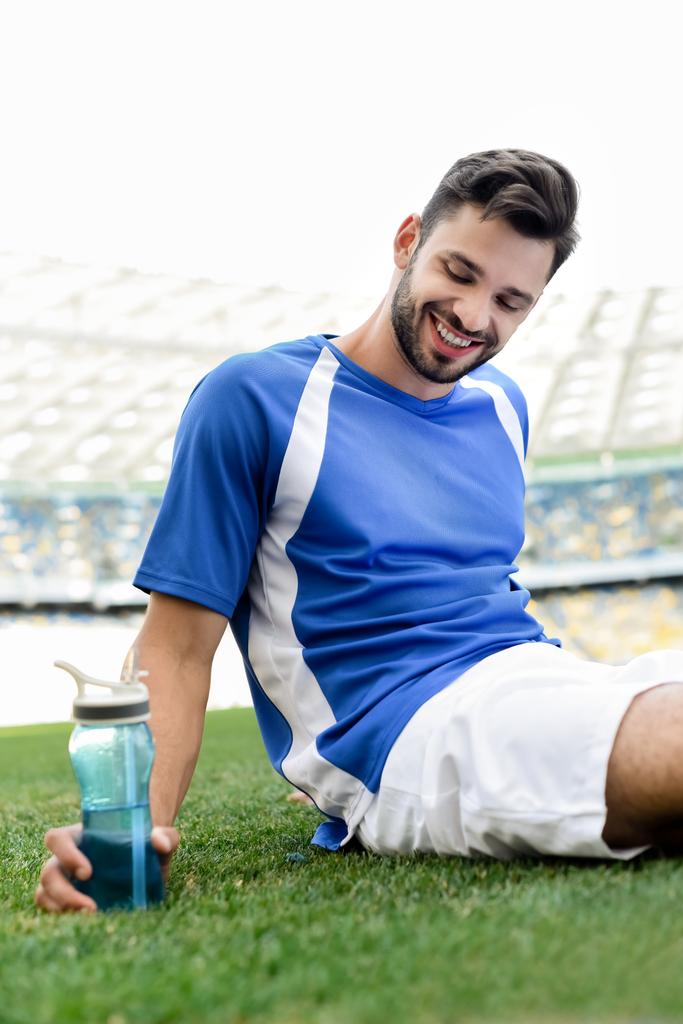 プロサッカー選手の笑顔が青と白のユニフォームを着てサッカーピッチに座って ロイヤリティフリー写真 画像素材