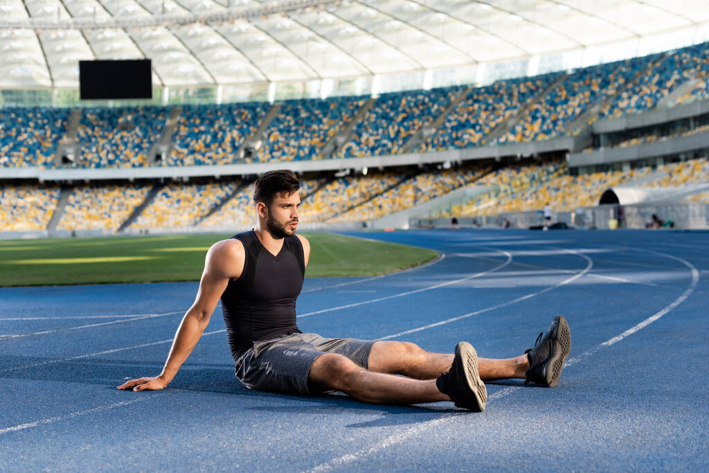 jóképű sportoló pihen a futópályán a stadionban - Fotó, kép