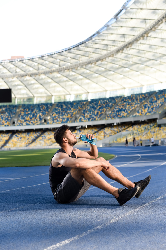 apuesto deportista descansando y agua potable en pista en el estadio
 - Foto, imagen