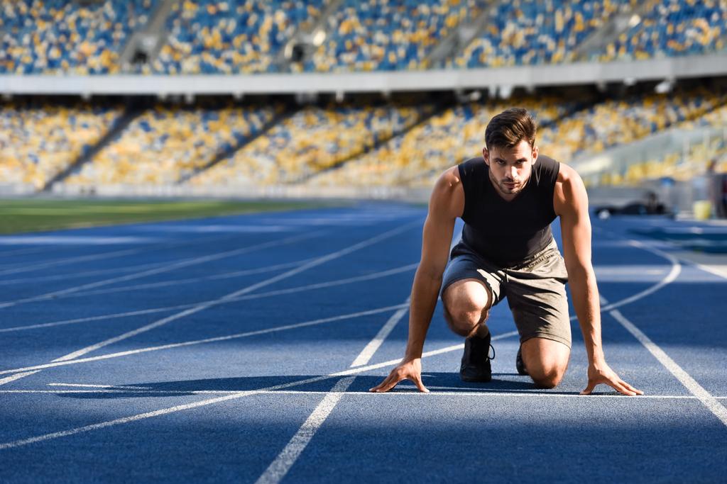 Stadyumdaki koşu pistinde başlangıç pozisyonunda yakışıklı koşucu - Fotoğraf, Görsel