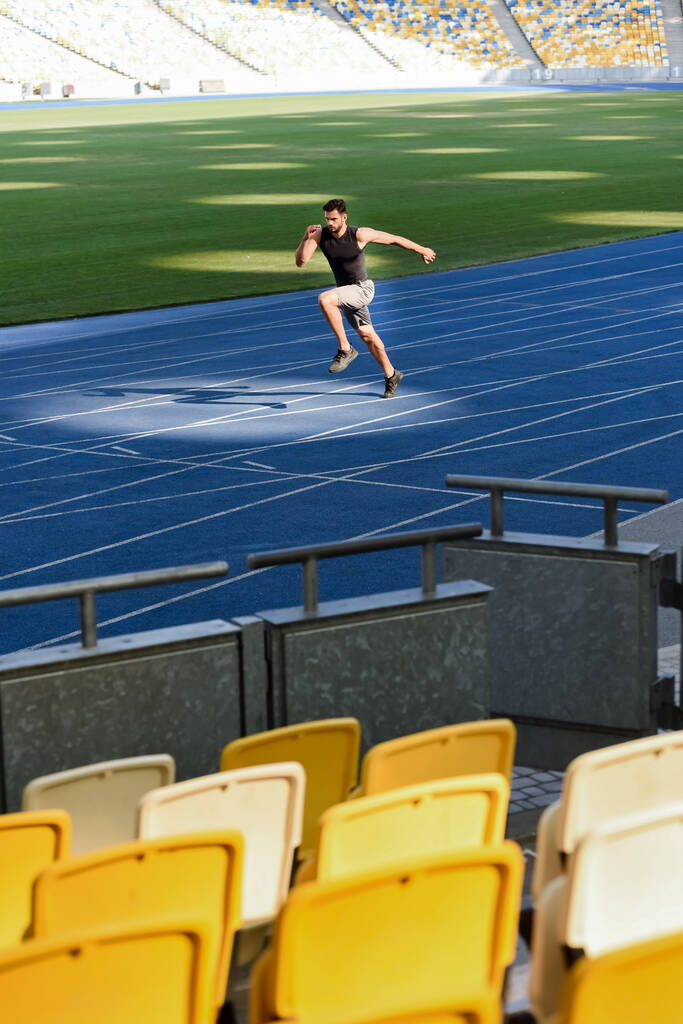 selective focus of seats and fast handsome runner exercising on running track at stadium - Photo, Image