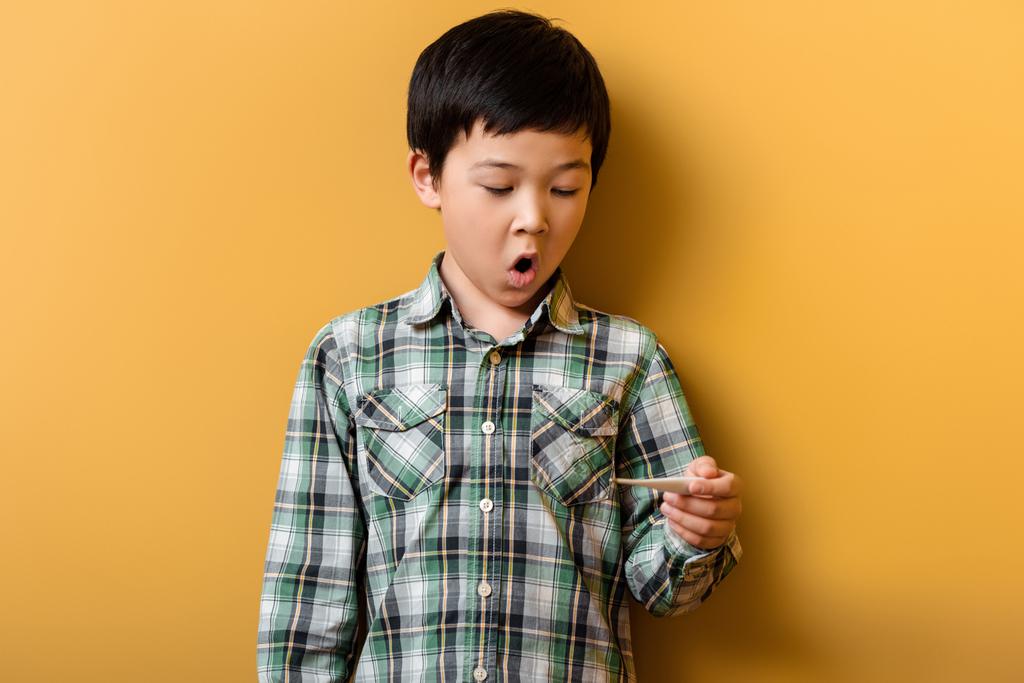 secoué un garçon asiatique tenant son thermomètre en jaune - Photo, image