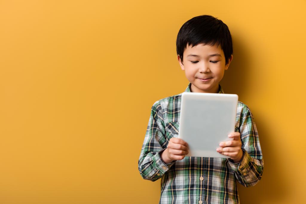 söpö hymyilevä aasialainen poika käyttäen digitaalista tablettia keltaisella - Valokuva, kuva