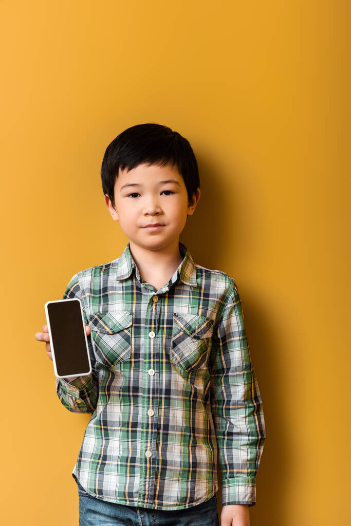 ázsiai fiú holding smartphone with blank screen on yellow - Fotó, kép