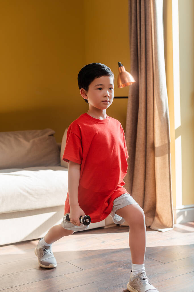 Мальчик занимается дома с гантелями во время самоизоляции - Фото, изображение