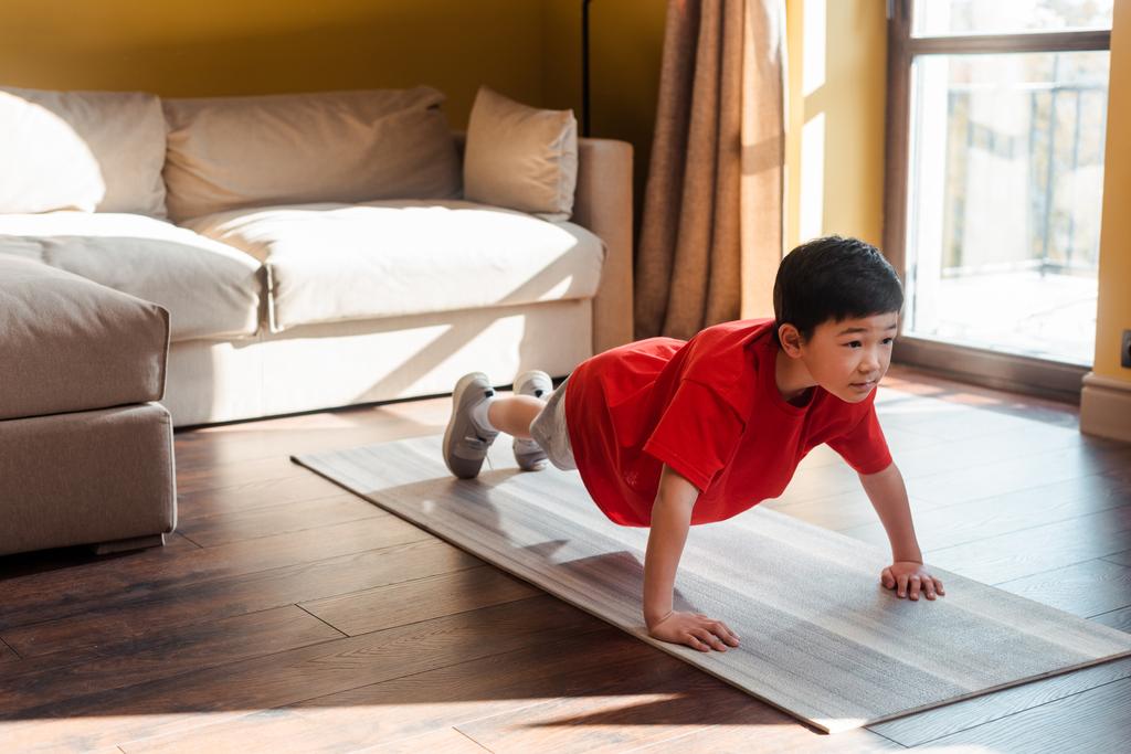 adorable sportive asian boy doing plank on fitness mat at home during self isolation - Photo, Image