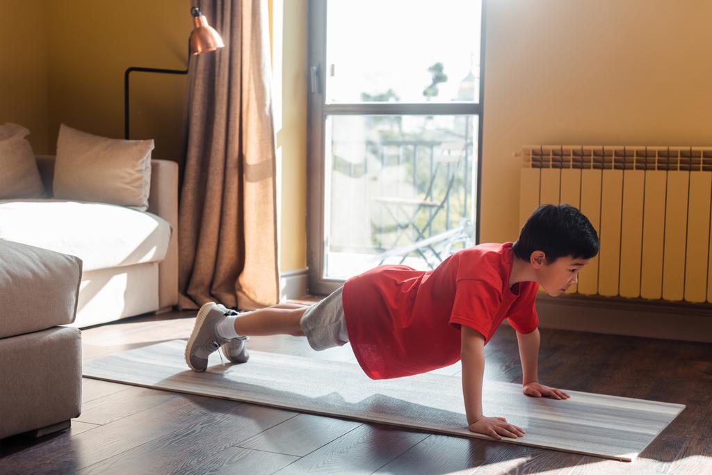 athlétisme asiatique un garçon fait une planche sur un tapis de conditionnement physique à la maison pendant son isolement - Photo, image