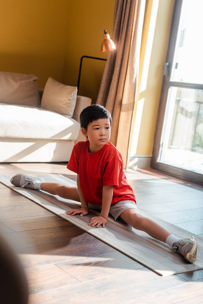 sportowy azjatycki chłopiec w sznurku poza na fitness mat w domu podczas kwarantanny - Zdjęcie, obraz