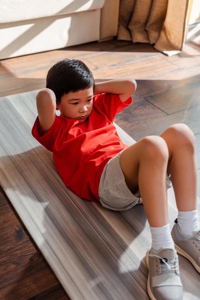 Un niño asiático deportista que hace abs en el gimnasio en casa durante el autoaislamiento. - Foto, imagen