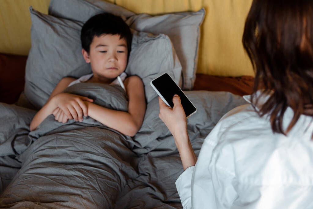 Hasta Asyalı çocuk yatakta yatarken annesi karantinada doktora sesleniyor. - Fotoğraf, Görsel