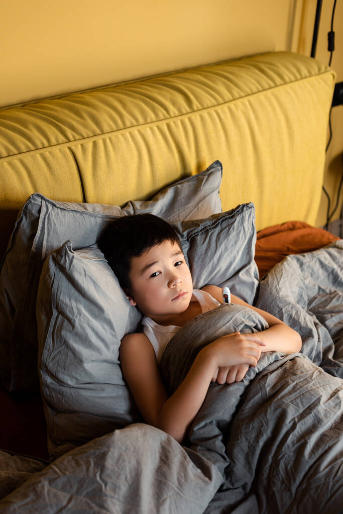 doente ásia menino com termômetro deitado no cama no quarentena - Foto, Imagem
