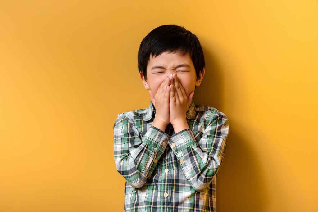 niño asiático enfermo estornuda en amarillo durante la cuarentena - Foto, Imagen