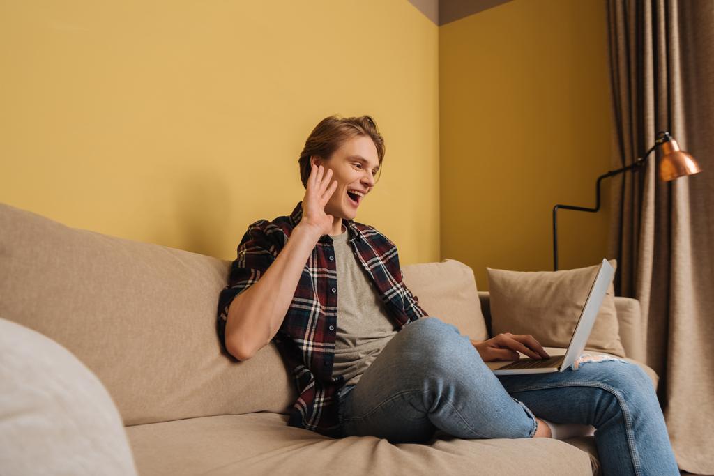 foco seletivo do homem alegre acenando a mão enquanto tem vídeo chat na sala de estar
  - Foto, Imagem