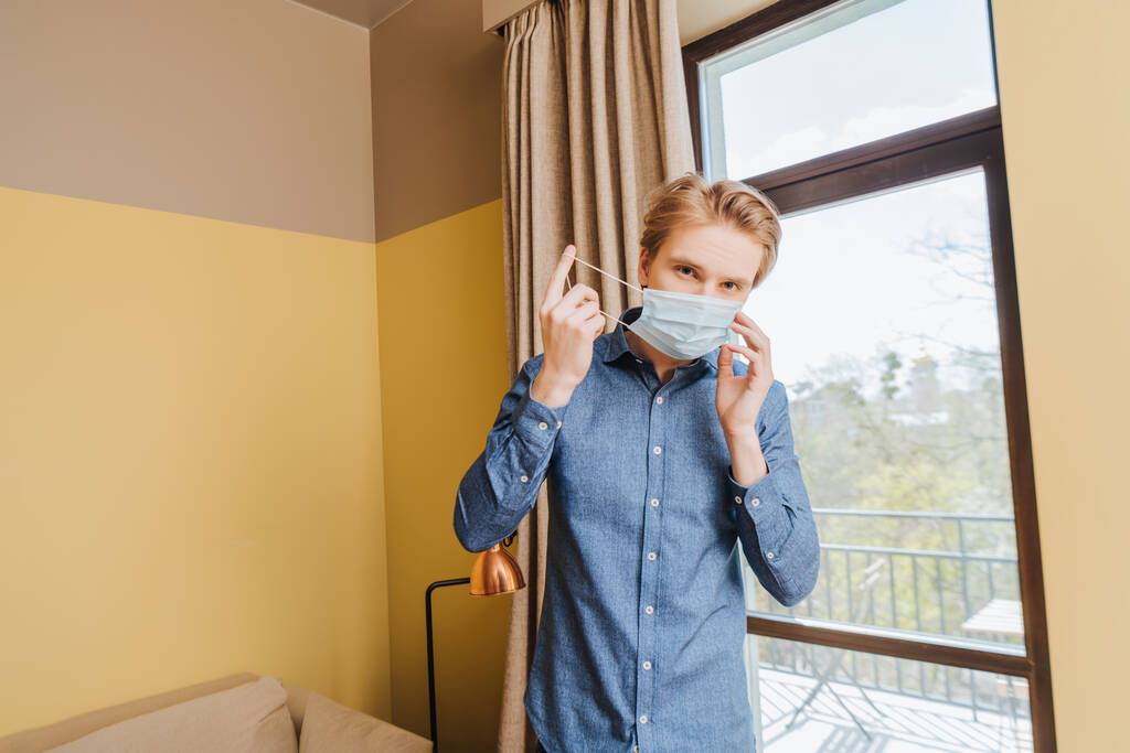 νεαρός άνδρας με μπλε ιατρική μάσκα στο σπίτι  - Φωτογραφία, εικόνα