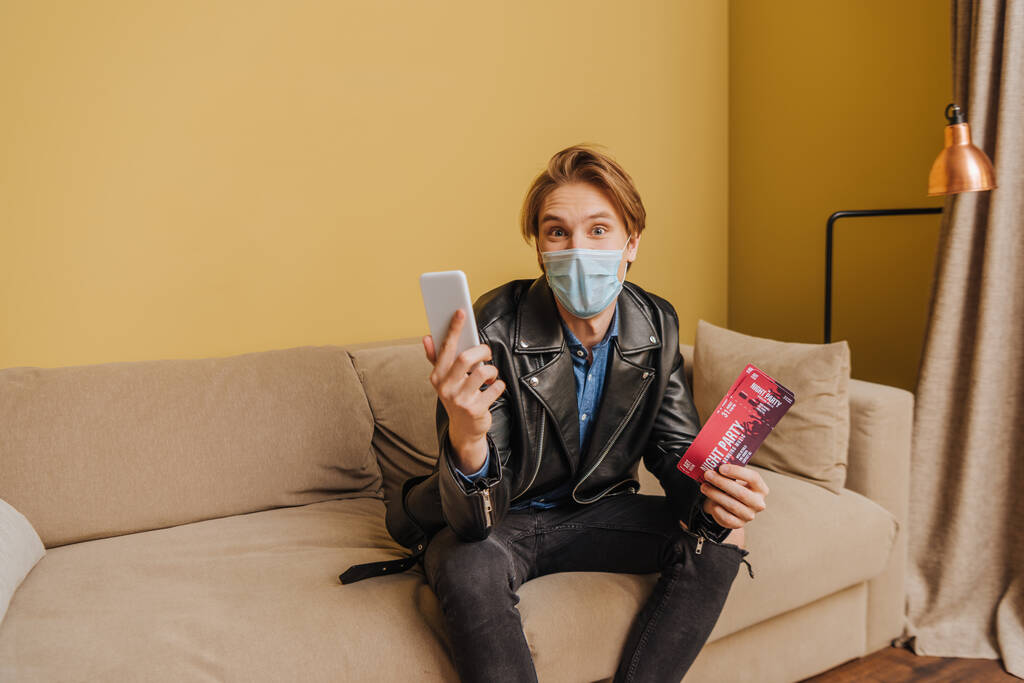 стильный мужчина в медицинской маске и пиджаке с ночными билетами и смартфоном, конец карантинной концепции
  - Фото, изображение