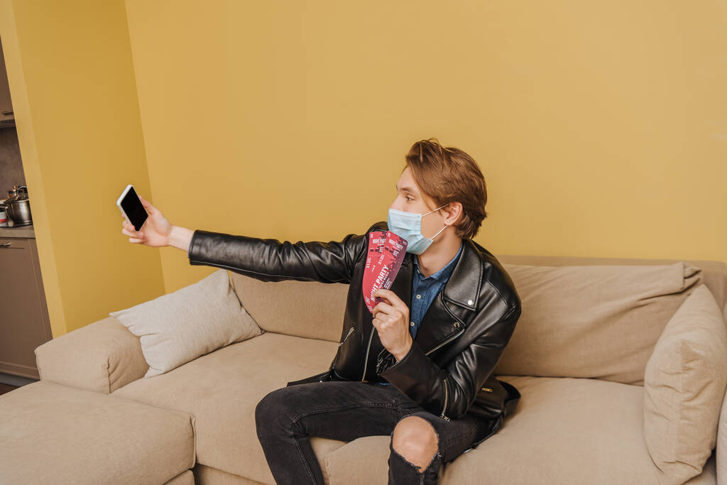 trendy man in medical mask and jacket holding night party tickets and taking selfie, end of quarantine concept  - Photo, Image
