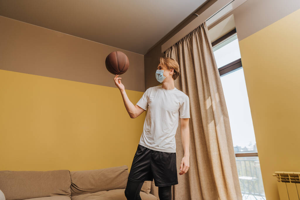 Tıp maskeli bir adam evde parmak üstünde basketbol oynuyor. - Fotoğraf, Görsel