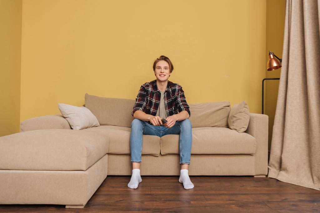 улыбающийся человек, держащий пульт дистанционного управления и сидящий на диване, конец карантинной концепции
  - Фото, изображение