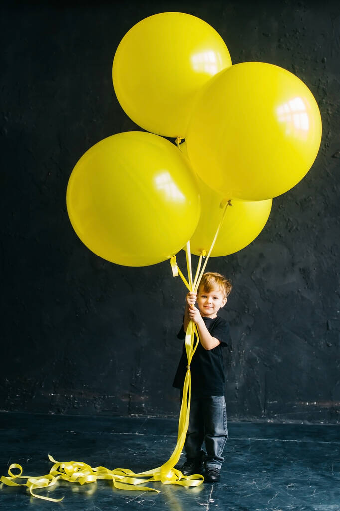 Мальчик рок-звезда с большими жёлтыми шариками. Стильный ребенок в черной одежде на черном фоне
. - Фото, изображение