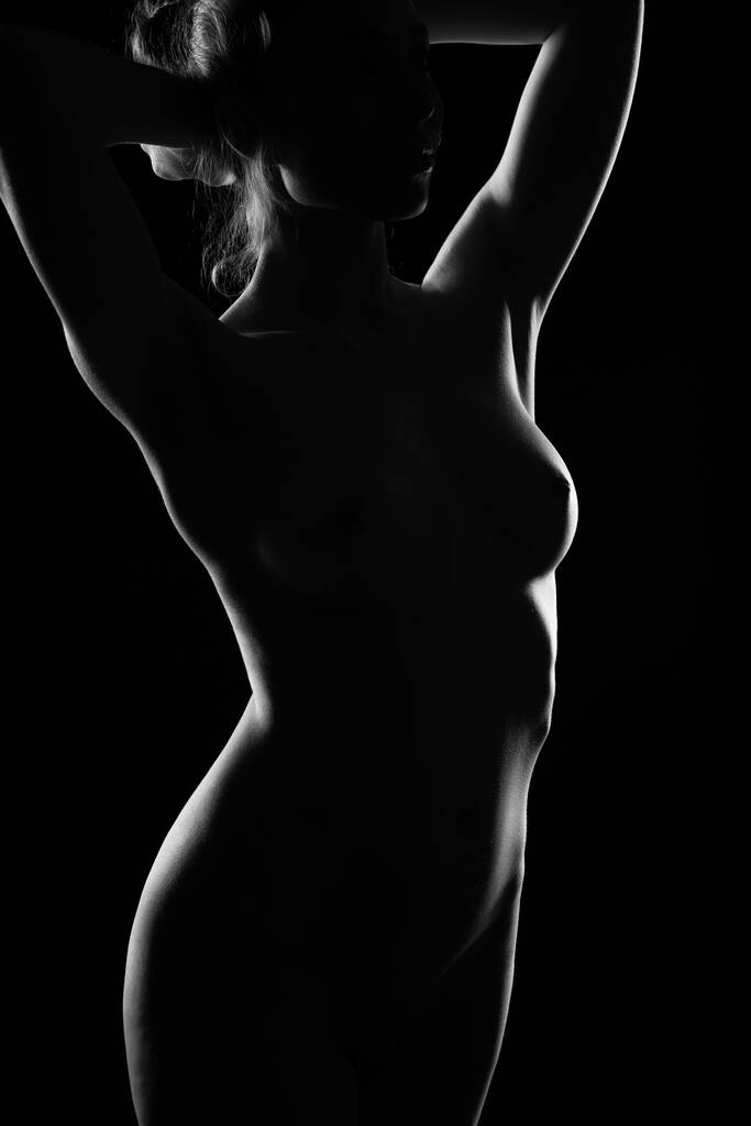 Karanlık bir arka planda çıplak bir kadın vücudunun ışık çizgisi. Çıplak kız saçını düzleştirir. - Fotoğraf, Görsel