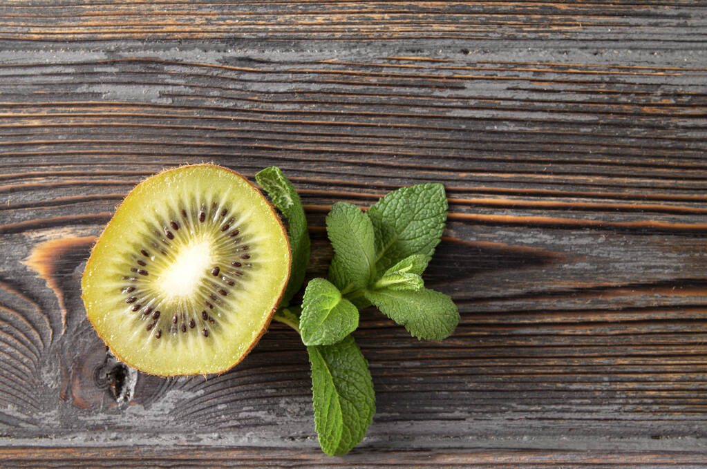 half of a fresh kiwi, a sprig of mint on a brown wooden background, top view - Photo, Image
