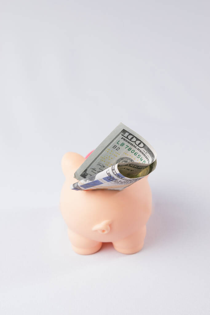Розовая свинья копилка на белом фоне. 100 долларов торчат из копилки
 - Фото, изображение