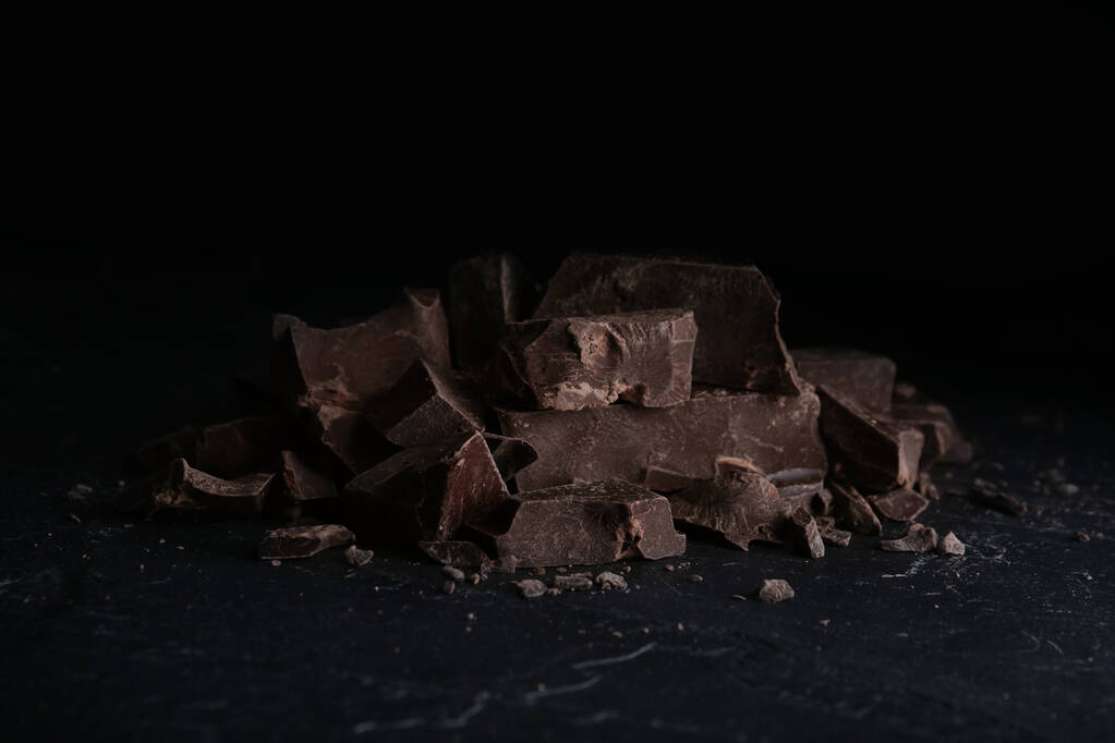 Kawałki smacznej ciemnej czekolady na czarnym stole - Zdjęcie, obraz