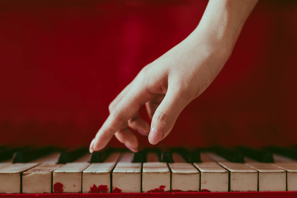 um close-up de uma vista lateral com a mão feminina com manicure rosa tocando piano. Um velho piano vermelho com teclas em preto e branco. Uma palma acima do teclado. Dedos graciosos de compositor ou músico
 - Foto, Imagem