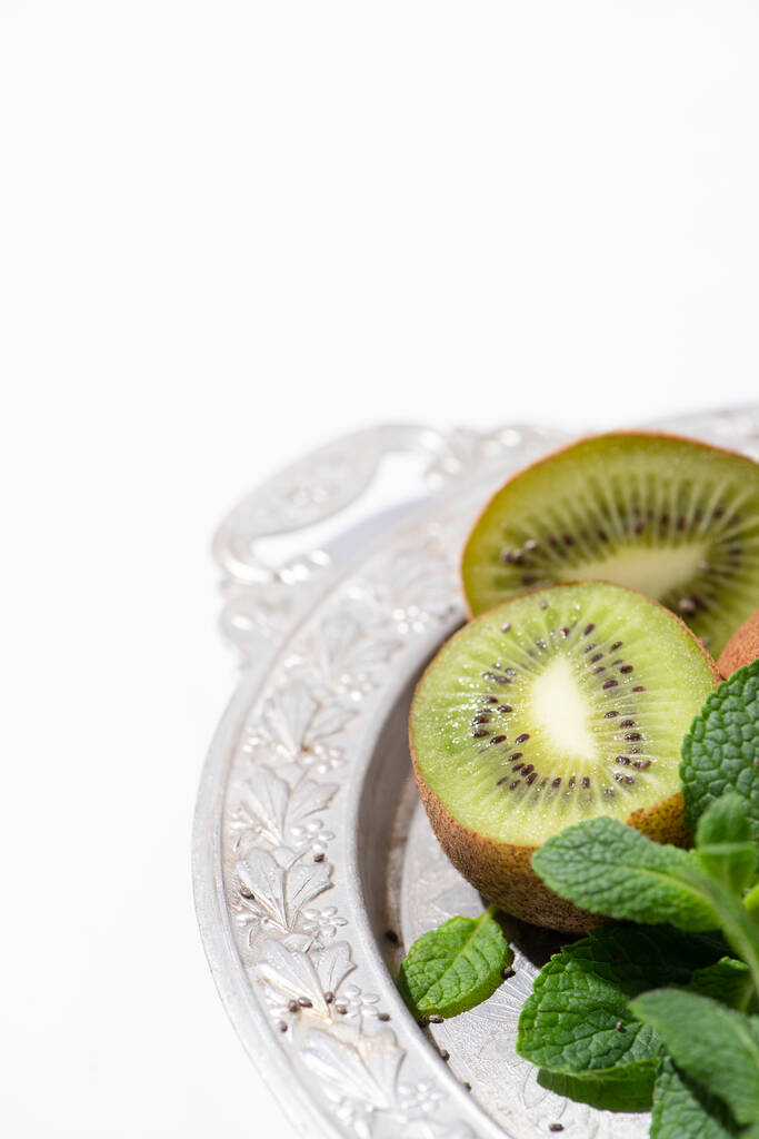 selective focus of tasty kiwi fruits near fresh and green peppermint on silver plate isolated on white - Photo, Image