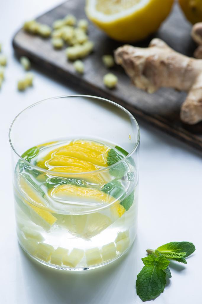 selective focus of fresh ginger lemonade in glass with lemon and mint on wooden board on white background - Photo, Image