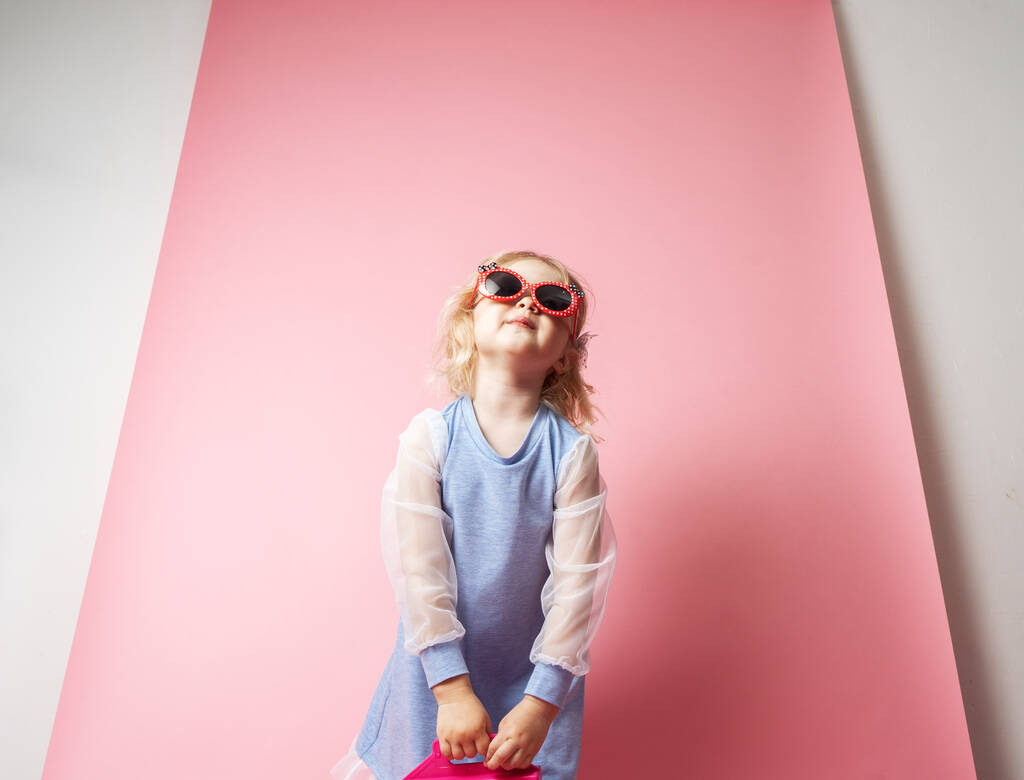 Little girl child in sunglasses with a pink redicle. Studio portrait on a pink background. - Photo, Image
