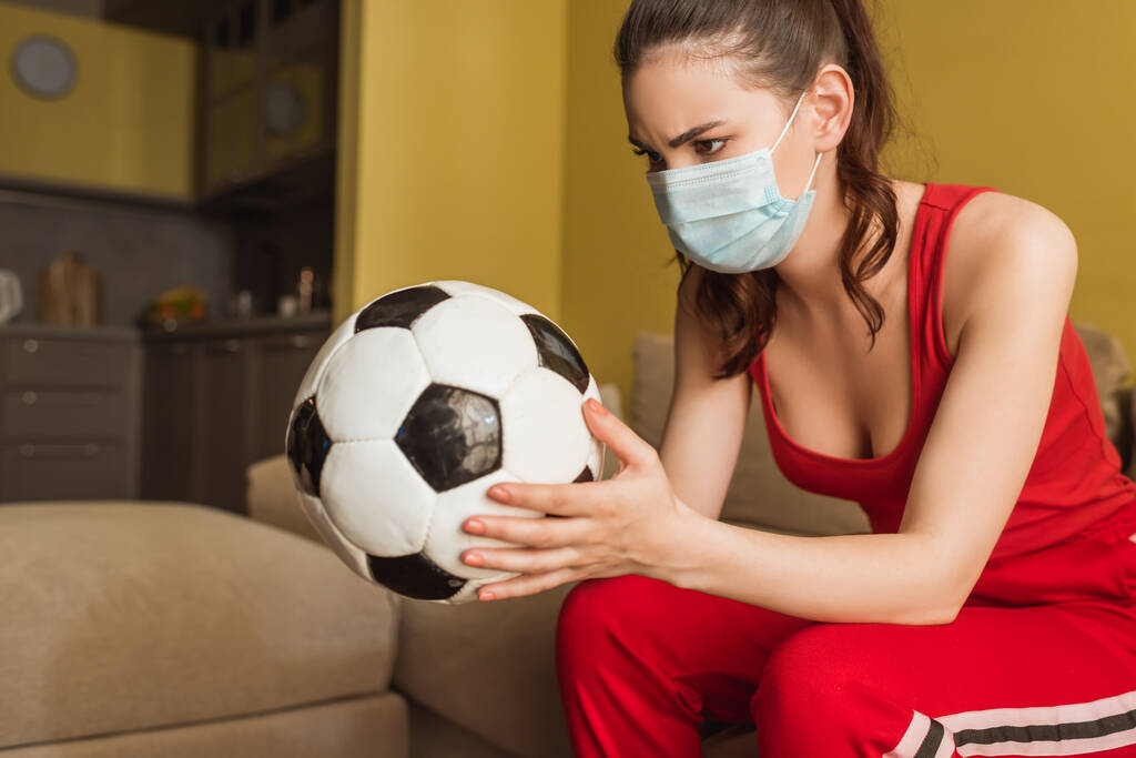sportieve vrouw met medisch masker kijken naar voetbal thuis - Foto, afbeelding