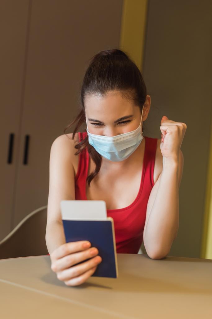 enfoque selectivo de chica feliz en máscara médica con pasaporte y billete de avión
 - Foto, Imagen