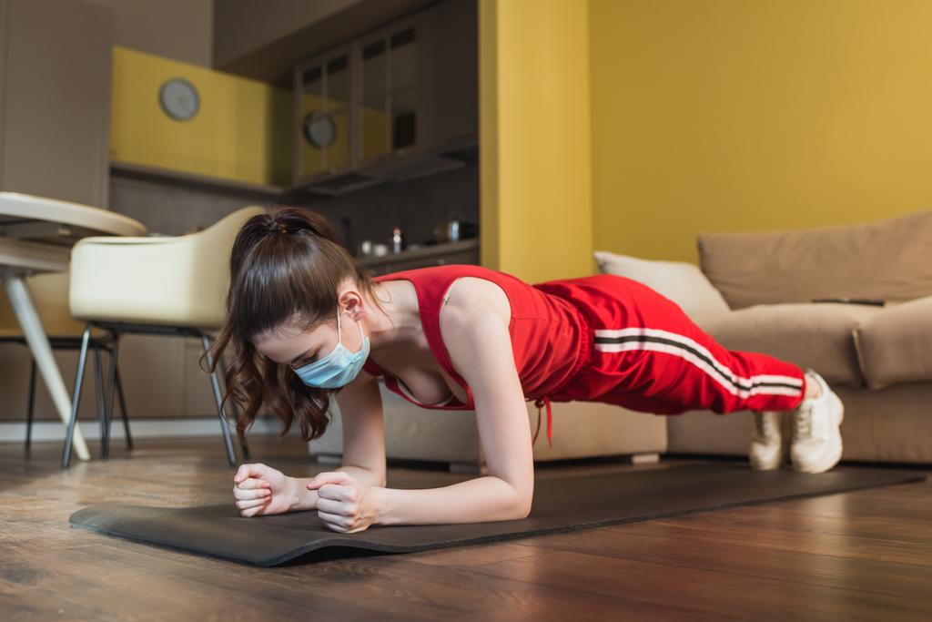 sportos nő orvosi maszk és sportruházat csinál deszka fitness mat  - Fotó, kép
