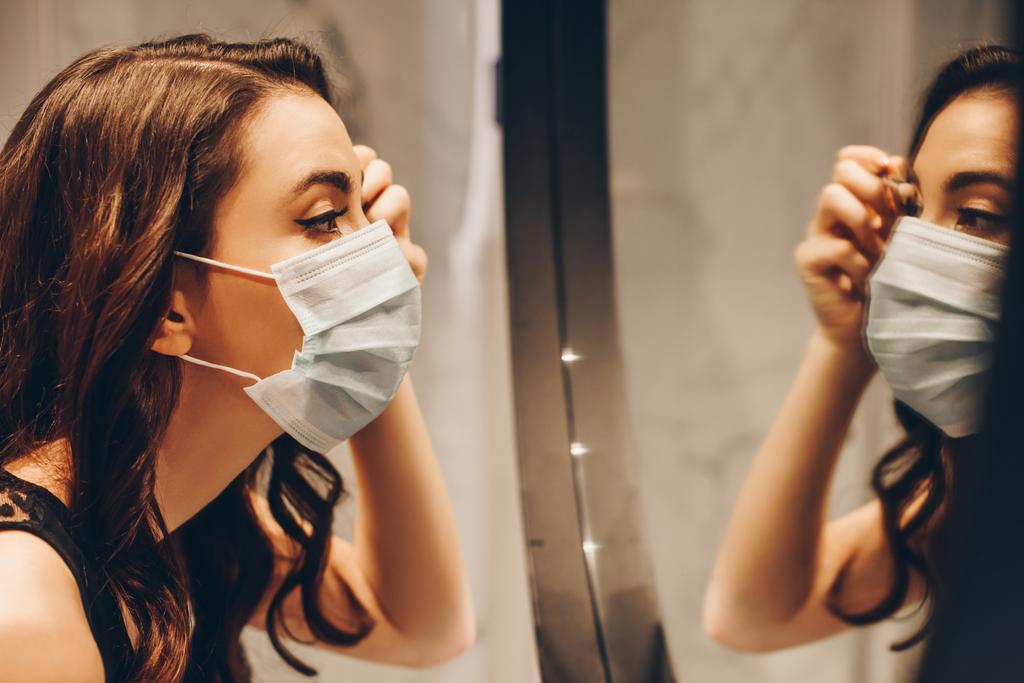 szelektív fókusz vonzó nő orvosi maszk alkalmazó szemhéjpúder a fürdőszobában - Fotó, kép