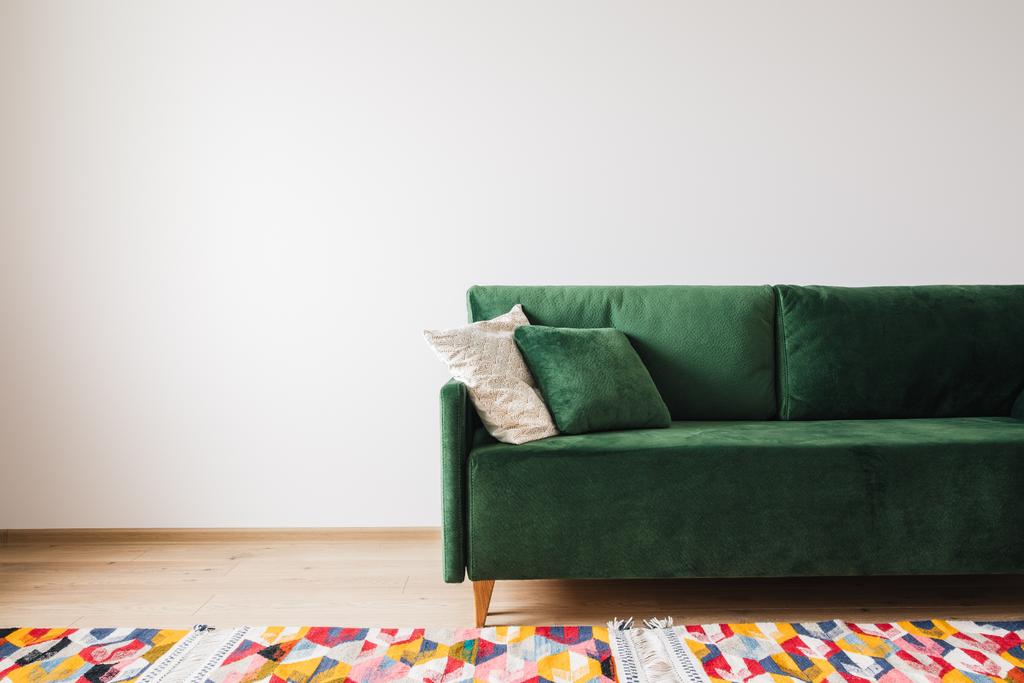 μοντέρνο πράσινο καναπέ με μαξιλάρια σε ευρύχωρο δωμάτιο με πολύχρωμο χαλί - Φωτογραφία, εικόνα
