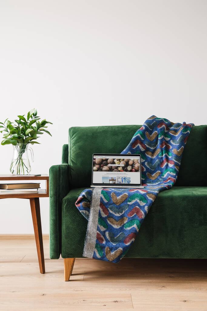 KYIV, UKRAINE -エイプリル社2020年14日:緑色のソファに毛布とノートパソコンを備え、預金写真付きウェブサイトを緑の植物と木製コーヒーテーブルの近くに設置 - 写真・画像