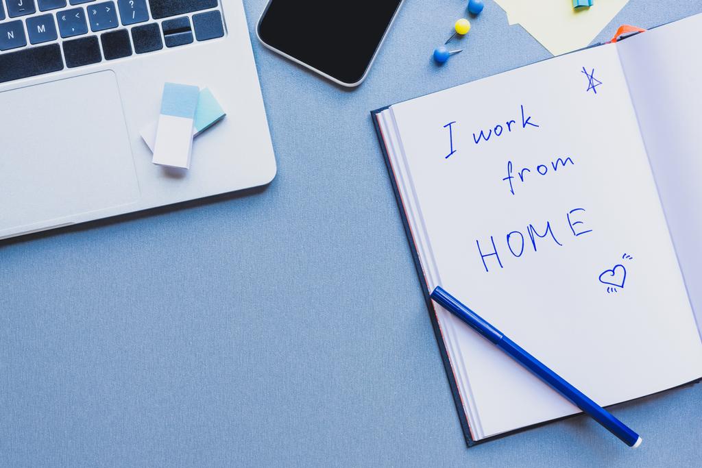 Draufsicht auf Gadgets, Bürobedarf und Schriftzüge Ich arbeite von zu Hause aus auf offenem Notizbuch auf blauer Oberfläche - Foto, Bild