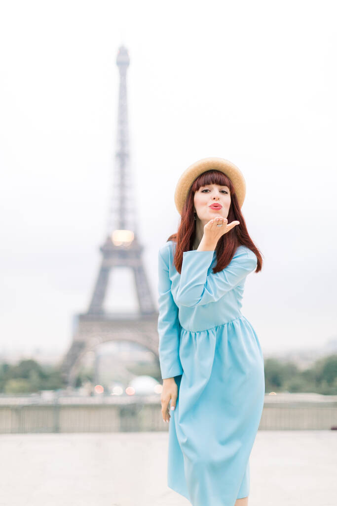 Eiffeltoren van Parijs. Mooie blanke vrouw met hoed en blauwe jurk, vrolijk glimlachend en luchtkus bij Trocadero uitkijkpunt voor Eiffeltoren in Parijs, Frankrijk - Foto, afbeelding