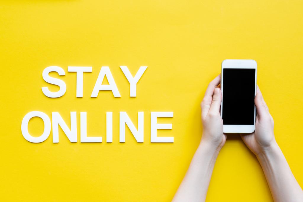 Top view of woman holding smartphone near stay online lettering on yellow background - Valokuva, kuva