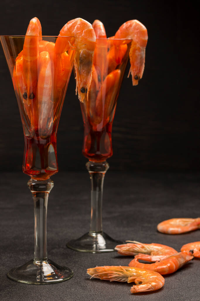 エビ入りオレンジグラス。テーブルの上のエビ。健康的な食欲をそそる食べ物。黒の背景 - 写真・画像