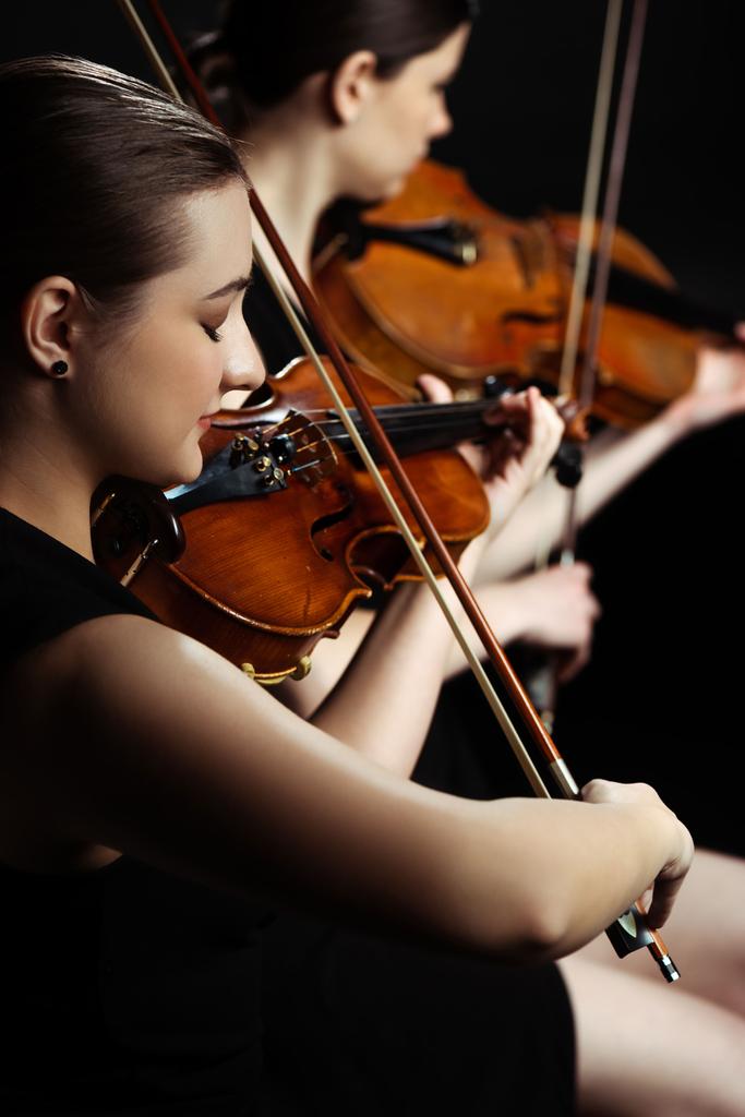 professional female musicians playing classical music on violins on dark stage, selective focus - Photo, Image