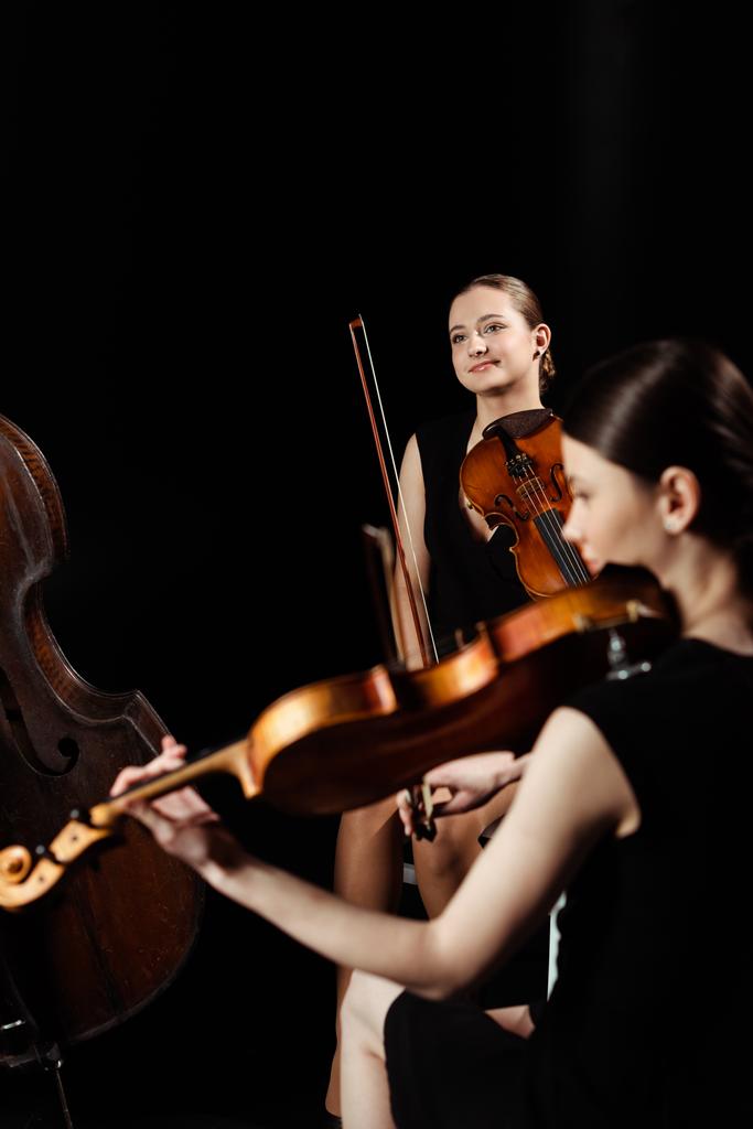 músicos positivos profissionais tocando música clássica em violinos no palco escuro
  - Foto, Imagem